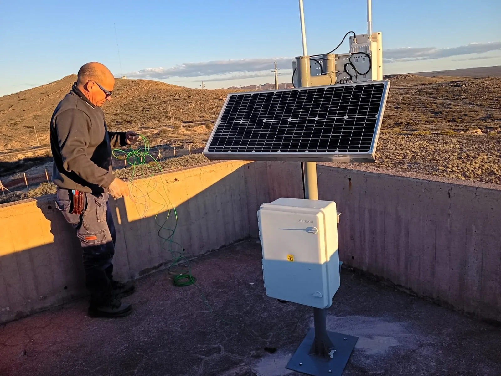 Técnico de Bitagonia junto a una estación de monitoreo con panel solar, gabinete y antena, instalada en una terraza de hormigón en la meseta