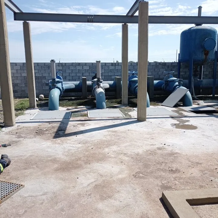 Planta de bombeo con cañerías azules, tanque hidroneumático y cerco de bloques a cielo abierto